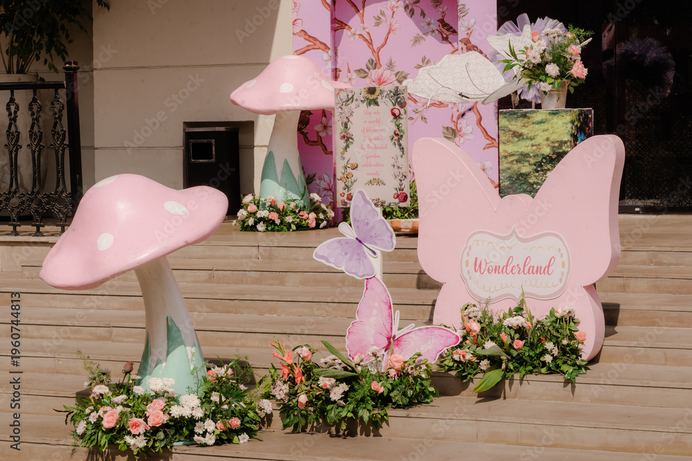 Fototapeta premium Enchanting outdoor whimsical party decorations featuring pink mushrooms, delicate butterflies, and lush floral arrangements on wooden steps in natural light
