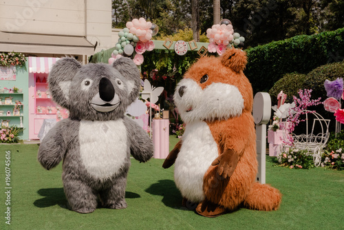 Canvas Print Two adorable animal character mascots, a koala and a groundhog, stand outdoors o