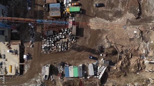 Aerial drone shot looking straight down at construction site yard with tower crane, stacked materials, vehicles, and dirt roads, illustrating logistics, storage, and industrial workflow.