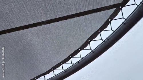 gray mesh or fabric screen attached to a frame possibly a trampoline edge, a fence, or a privacy screen against an overcast sky.