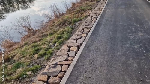 reinforced bank embankment with path stabilize slope and protect against erosion. Stone retaining wall, bank is reinforced with dry stone wall holds soil and prevents it from sliding into water.