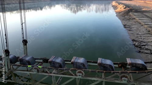 bucket chain excavator massive piece of industrial equipment typically used in open-pit mining or large-scale dredging. operating at edge of water body, likely excavating material from shoreline or fl