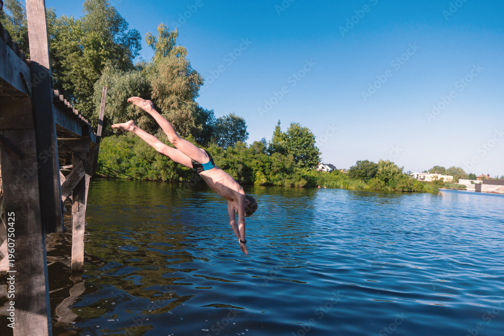Fototapeta premium Young Boy Diving Headfirst into Calm Lake from Wooden Pier on Sunny Summer Day