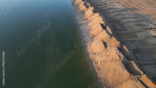 Extensive earthworks and material extraction are underway at site.truck is seen transporting sand or gravel along the water surface. project involves building infrastructure to connect channel, rial v