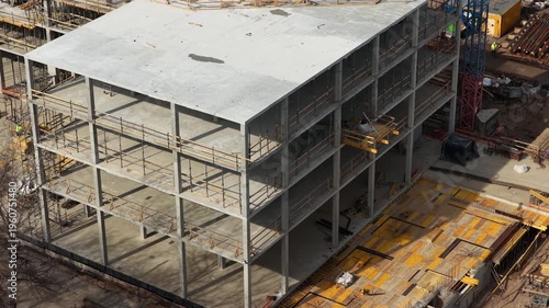 Drone footage capturing a partially completed multi story concrete building with scaffolding, formwork, and materials, highlighting structural progress and active construction environment.