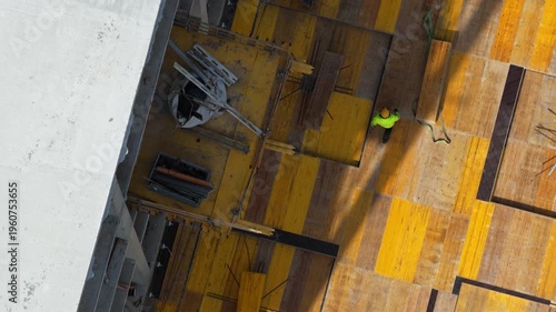 Aerial drone shot looking straight down at two construction workers installing steel reinforcement on formwork deck, showcasing structural preparation and active building process.