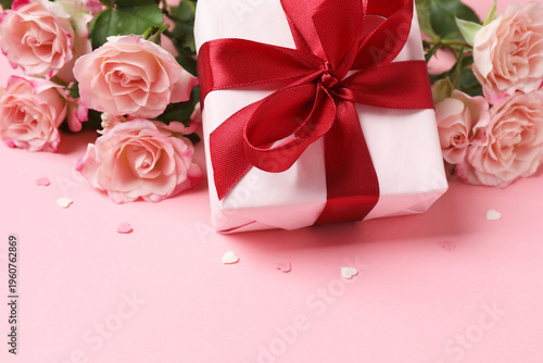 Beautiful pink roses with gift box with ribbon on pink background

