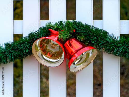 white fence with christmas decoration made by a green garland and two red metallic glossy bells