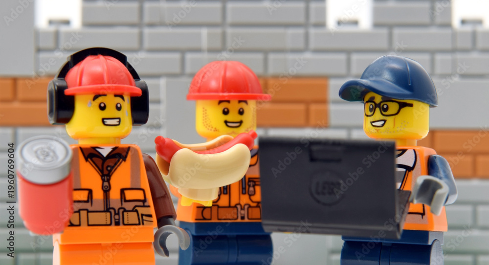 Fototapeta premium Lego minifigures of workers in redheads and engineer with laptop against a brick wall. Editorial illustrative image of popular children toys and people occupation.