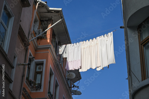White bed linen is being dried on a clothesline stretched between houses