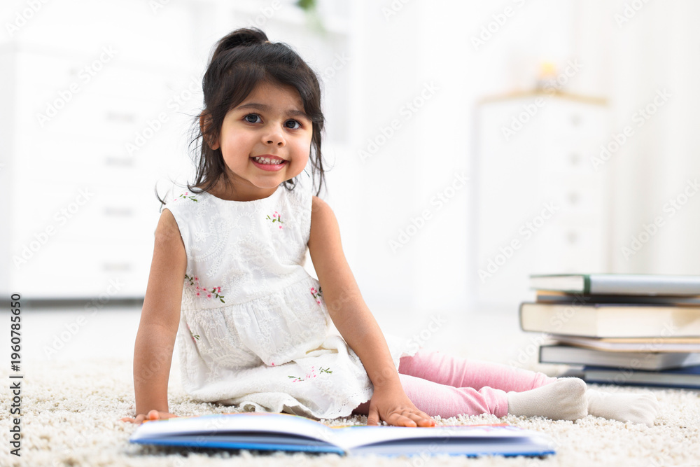 Obraz premium Cute little girl reading book on floor at home. Space for text