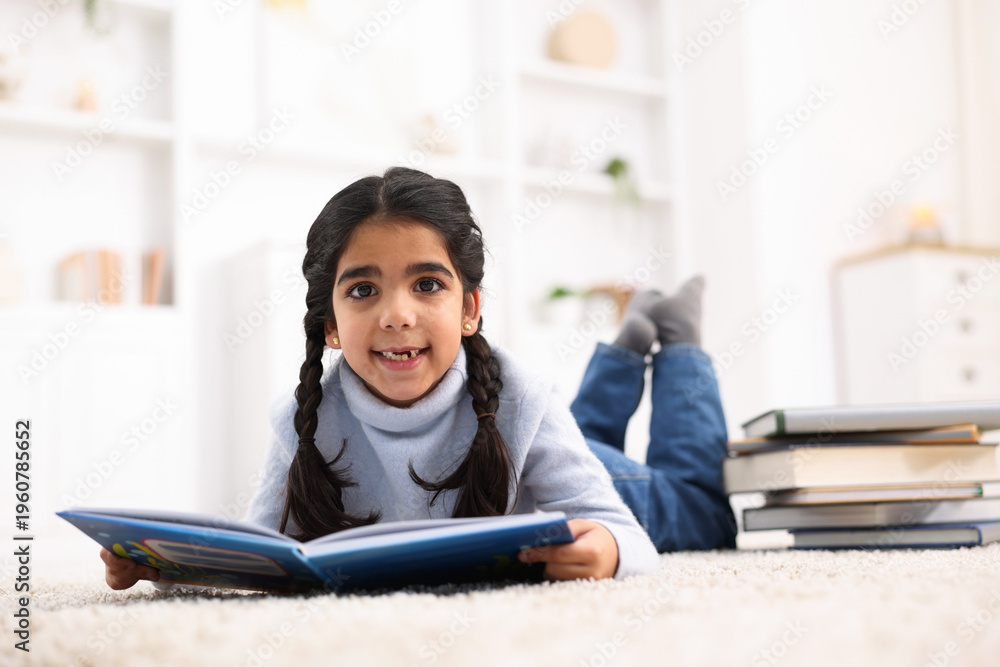 Obraz premium Cute little girl reading book on floor at home