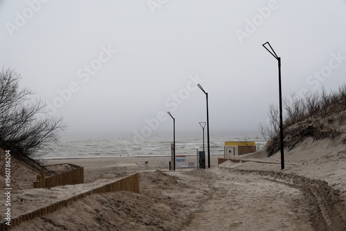 Foggy coastal scene with dunes, lamps, and empty shoreline view