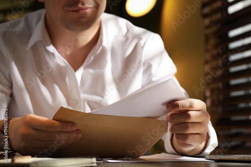 Tableau sur toile Man putting letter into envelope at wooden table indoors, closeup