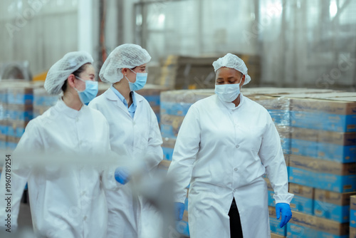 Billede på lærred Multinational female workers walk together in canned fish factory discussing workflow and production process