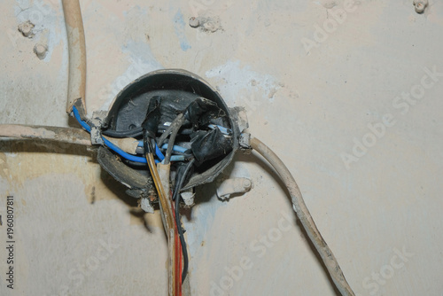 Close-up of an open electrical junction box with exposed wires and taped connections on a damaged wall. Concept of electrical hazard, poor wiring, home maintenance issues, and safety risks in resident