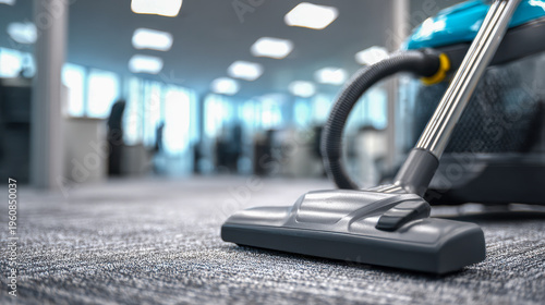 Vacuum cleaner head cleaning a carpeted floor in a modern office space with natural light and blurred background showing desks and windows