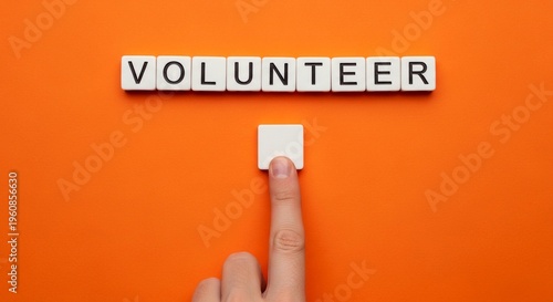 Finger pointing at a blank square tile below the word 'VOLUNTEER' on an orange background.