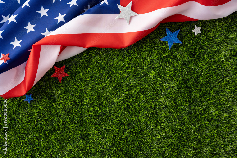 Fototapeta premium Wavy American flag and glitter stars laid on green grass evoking patriotism, summer holidays, and national pride for Independence Day, Memorial Day, Labor Day and other USA celebrations