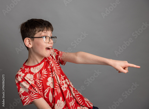 boy in glasses pointing at camera with excited expression on grey background