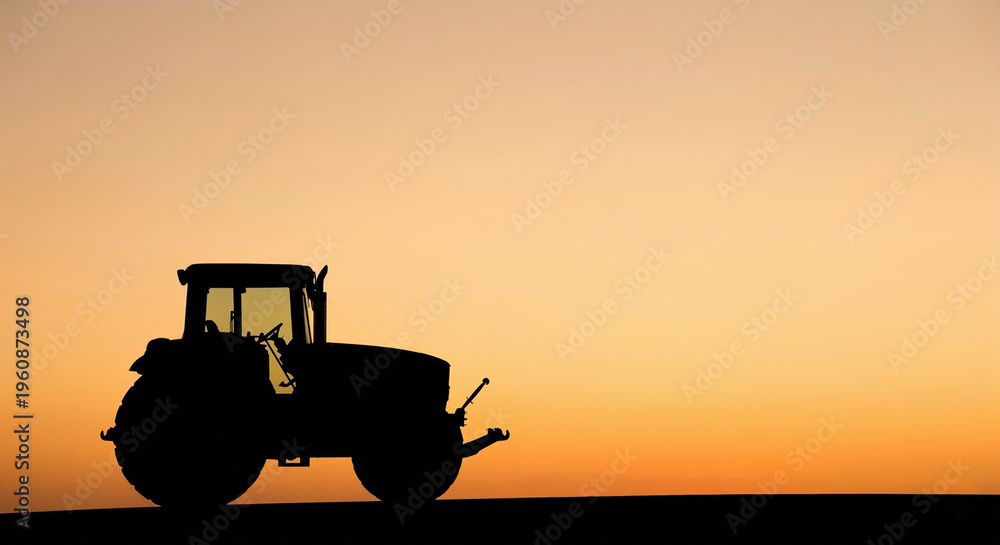 Fototapeta premium Silhouette of a Farm Tractor Against a Beautiful Golden Sunset Sky