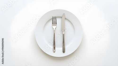 Top view of empty white ceramic plate with silver fork and knife on white background