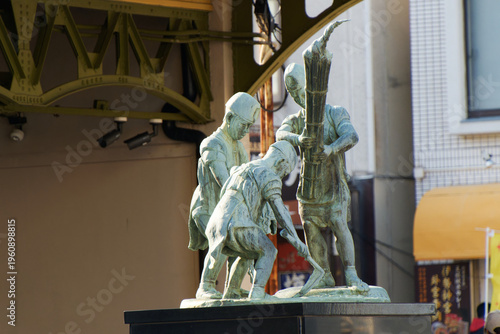 Fotografi Bronze statue of traditional harbor workers at Mojiko port historical site under sunlight in Japan