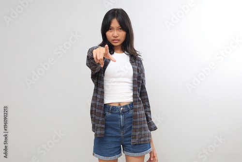 Photos An Asian teenage girl isolated on a gray background, looking frustrated and angry while pointing forward