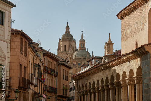 Charming street scene in the historic center of Segovia with traditional architecture, arcaded buildings, and a view of the iconic Segovia Cathedral rising above the rooftops. 