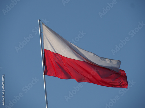 Polish white and red banner waving on a pole against a cloudless blue sky