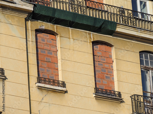 Detailed view of two bricked up window openings on an old yellow facade