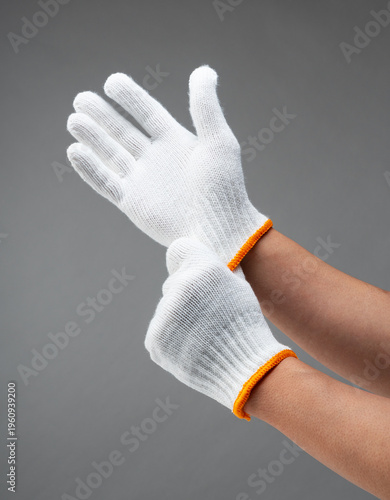 Two hands wearing white cotton work gloves on gray background