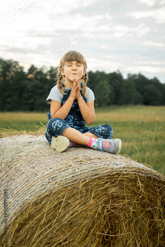 Cheerful little girl sitting on a haystack with her eyes closed