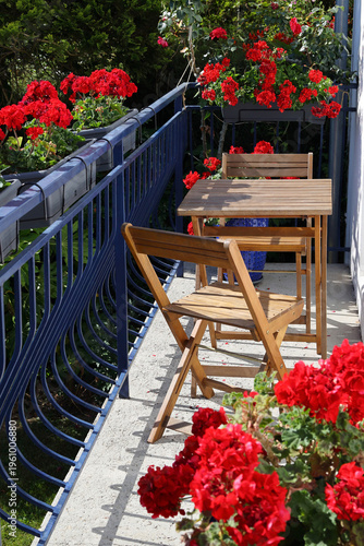 Wooden table and chairs on enchanting balcony adorned with vibrant red geraniums in full bloom