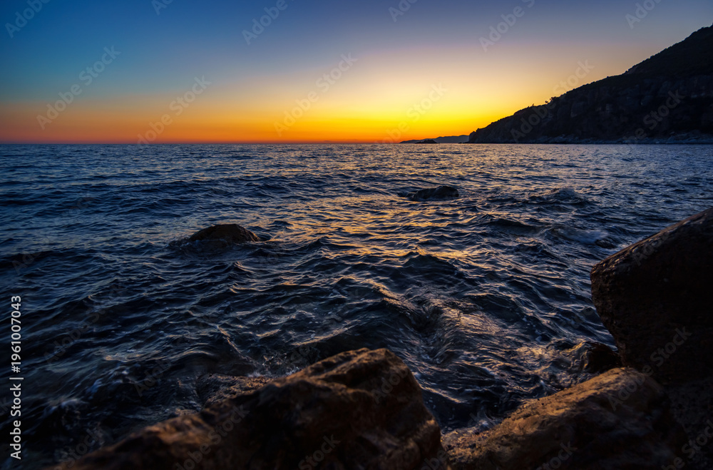 Obraz premium Atmospheric sunset over the dark waters and rocky coast of Petrovac, Montenegro. Dramatic summer travel scene.
