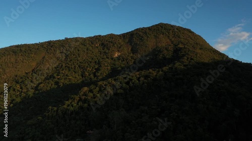 Aerial view of a dense tropical mountain forest at sunset with deep shadows and golden light on the canopy
