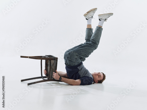 Foto Man lying upside down holding chair isolated on white background in unusual pose