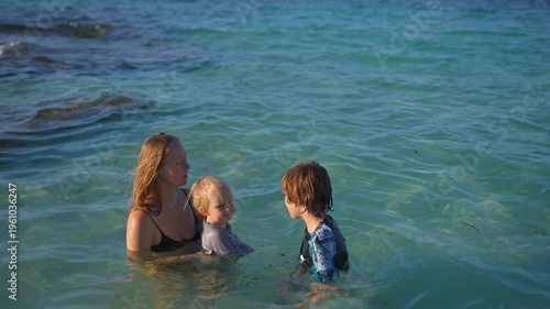 Young mom spending quality time with her two sons on a beautiful tropical beach, enjoying sunshine, laughter, and family bonding moments by the sea.