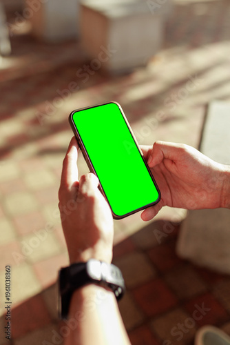 Close up of hands holding a smartphone with a chroma key green screen outdoors