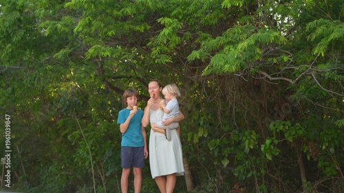 Young mom spending quality time with her two sons in a lush green park, enjoying nature, laughter, and joyful family bonding moments outdoors.