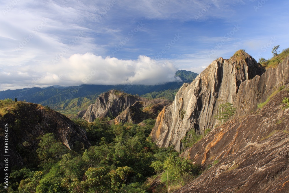 Fototapeta premium Stunning view of sharp, jagged rock formations surrounded by lush green hills under a cloudy sky