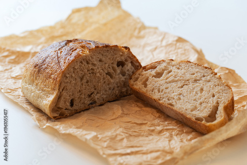 Obraz na płótnie Close-up of a sliced fresh sourdough bread loaf on brown parchment paper, isolated on a white background with soft natural side lighting