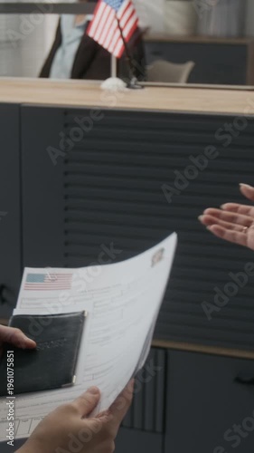 Over-shoulder vertical shot of anonymous woman and female friend checking documents, then submitting to USA embassy clerk while applying for American immigration visa
