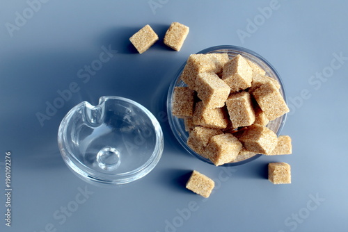 Photography A glass bowl with brown lump sugar stands on a grey background.