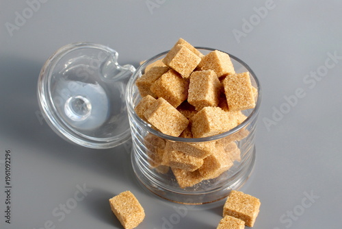 Photos A glass bowl with brown lump sugar stands on a grey background.