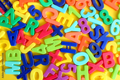 Abstract texture of many bright multi-colored letters lying on a yellow background.