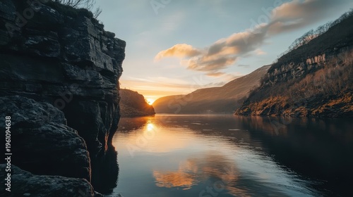 Serene sunset over calm waters, framed by majestic cliffs and hills in tranquil landscape.