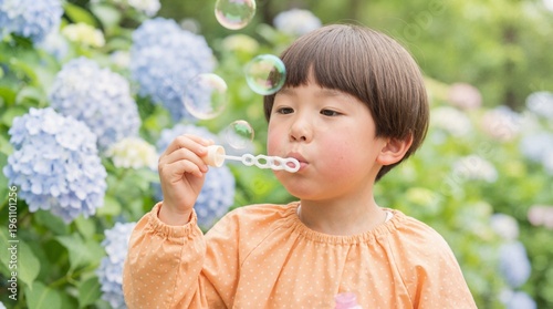 Japanese child blowing bubbles in a hydrangea garden. Young kid playing among blue flowers outdoors. Summer childhood activity concept