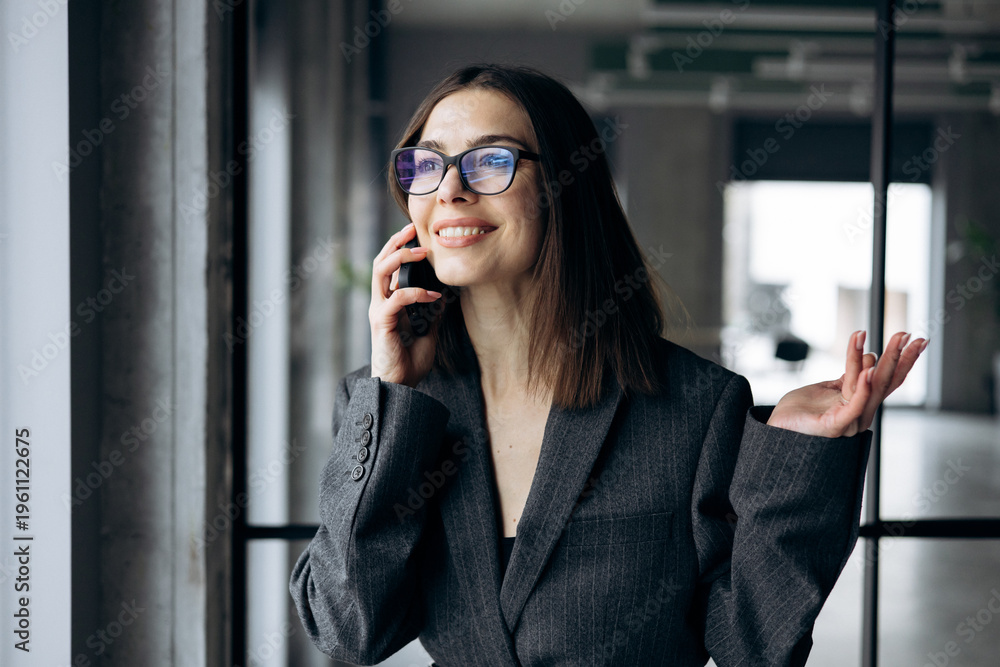 Fototapeta premium Business woman standing at the office window and talking on the mobile phone
