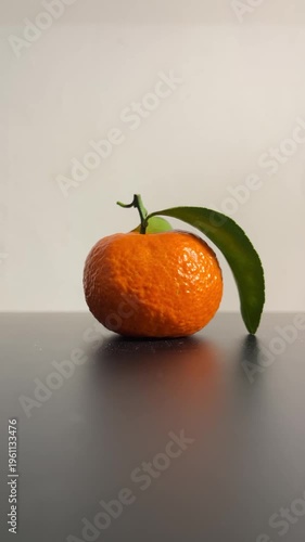 Fresh ripe tangerine with green leaf on a dark surface in a minimal setting. Ideal for concepts of healthy food, freshness, simplicity, and wellness.